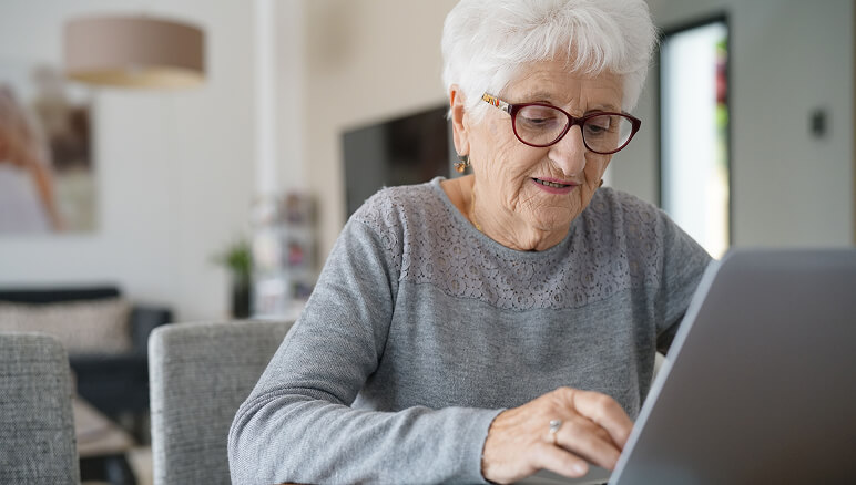 Woman with glasses using a tablet at a table in a cozy, bright living room
