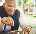 Man smiling while playing chess outdoors on a wooden table. 