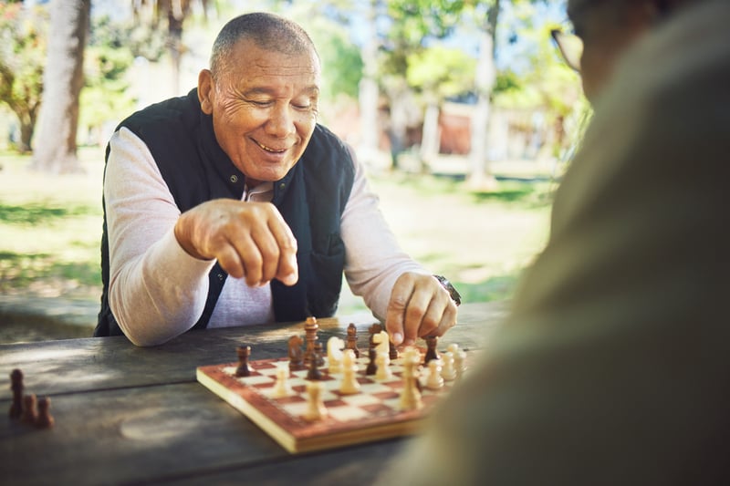 Two men playing chess in a park, focused on the game while seated at a picnic table under a tree