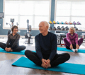 Adults sit smiling on yoga mats in a bright fitness room.