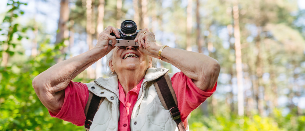 Smiling senior woman taking photo on nature walk. - Article Module