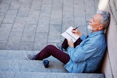 Top view of a senior man sitting outside and writing to do list