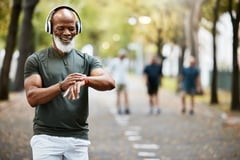 smiling older athlete standing in park mid-run looking at wearable fitness tracker device on wrist