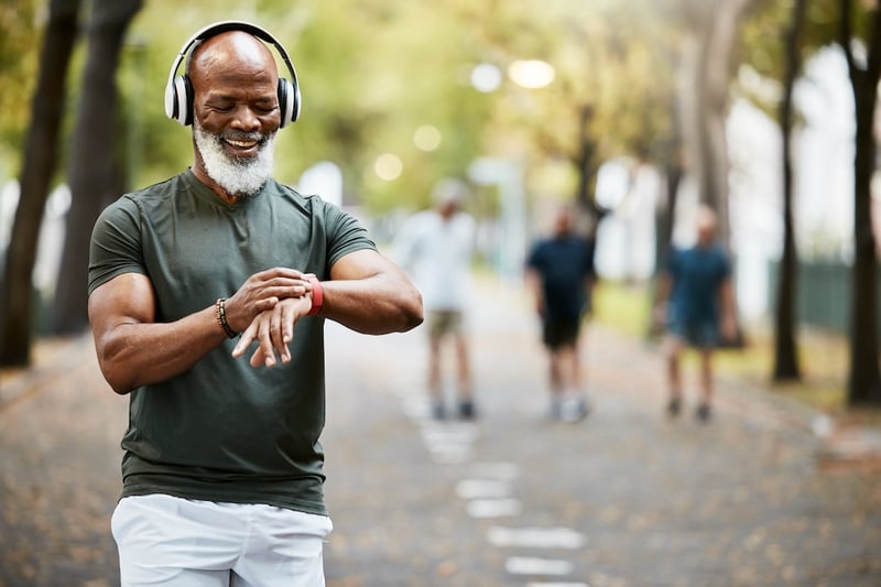 smiling older athlete standing in park mid-run looking at wearable fitness tracker device on wrist